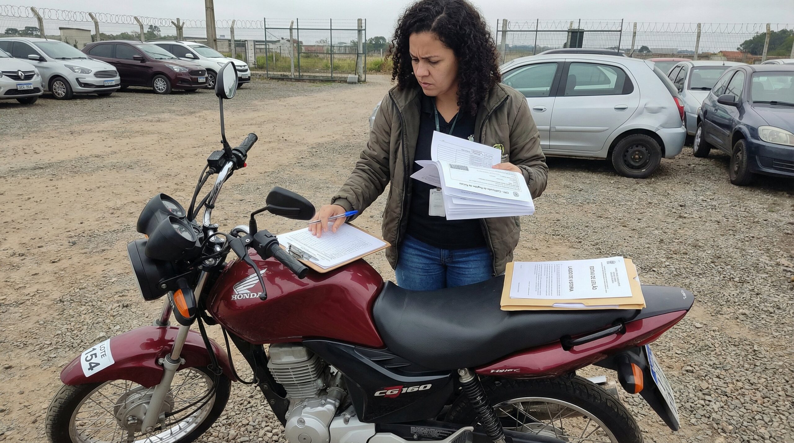 Mulher verificando documentos CRV e laudo de vistoria ao lado de moto Honda CG arrematada em leilão com checklist na mão