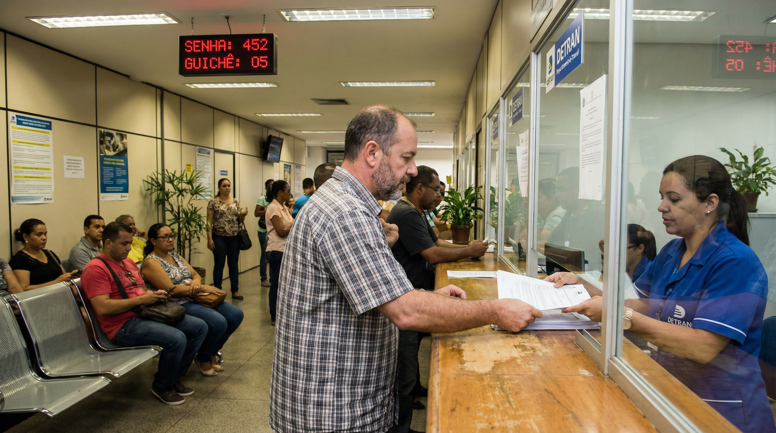 Homem brasileiro no balcão do DETRAN preenchendo documentos de transferência veicular com atendente