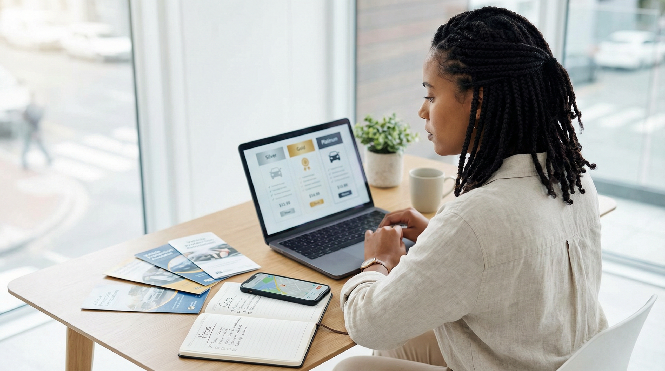 Mulher brasileira comparando planos alternativos de proteção veicular no laptop com folhetos de associações e app de rastreamento no celular